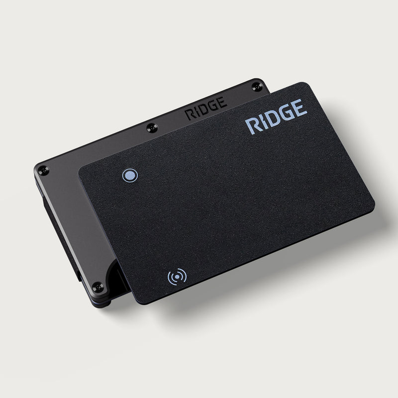 Tracker Card in black leaning against its black metal wallet, both with Ridge logo, on a plain background.